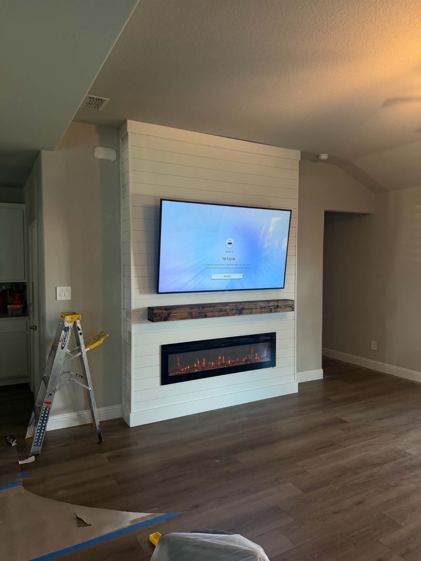 Completed white custom media wall with television, fireplace, and wood mantel