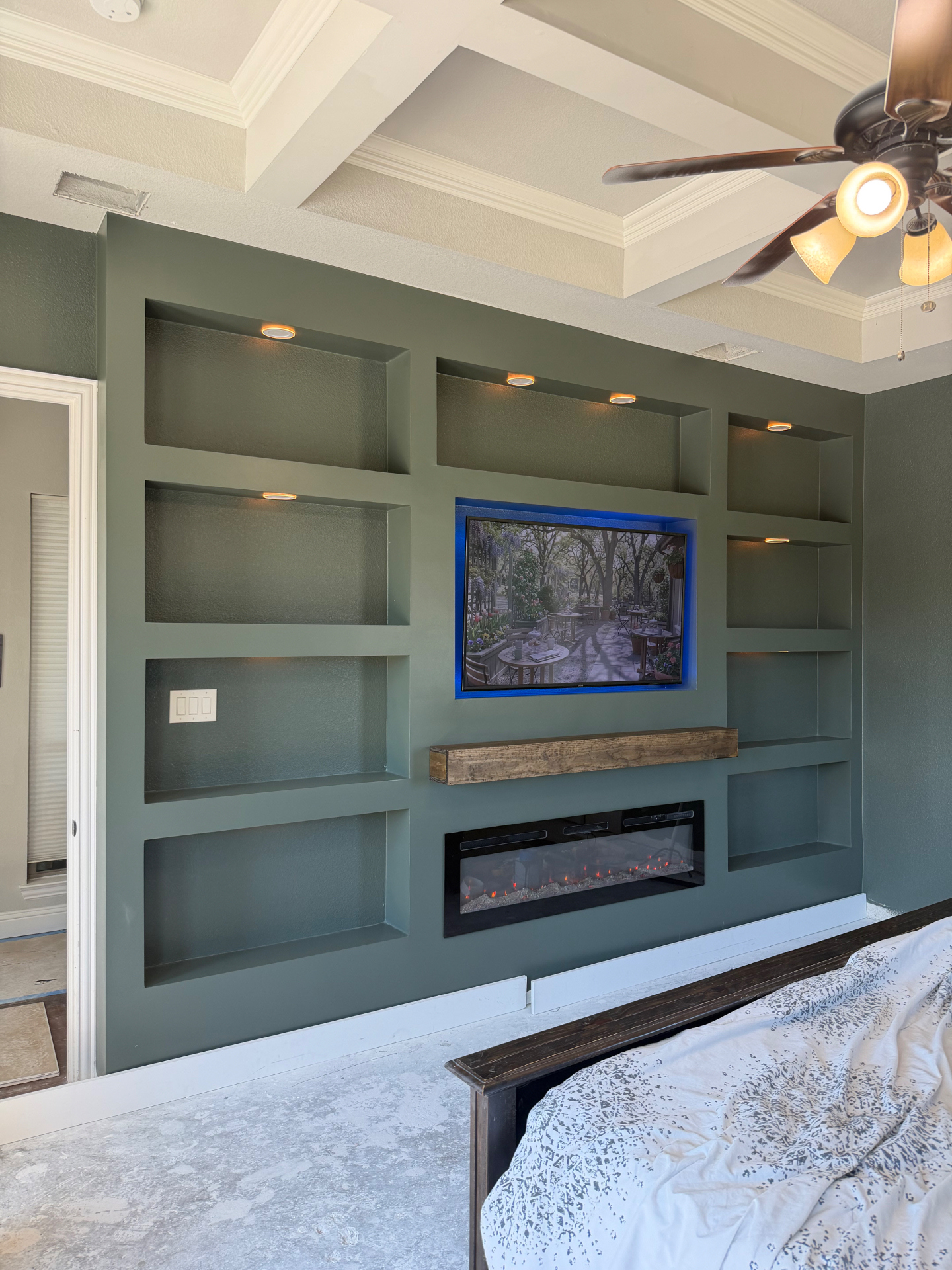 Finished built-in media wall with lit shelves, TV, wood mantel and fireplace