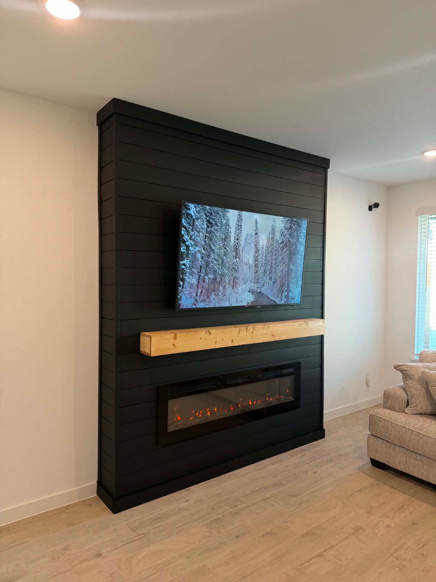 Completed black custom media wall with television, fireplace, and wood mantel